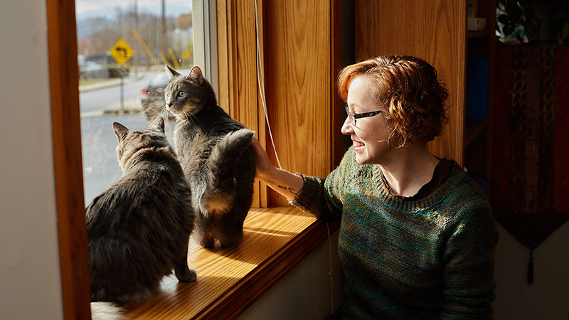Woman looks out of window with two cats