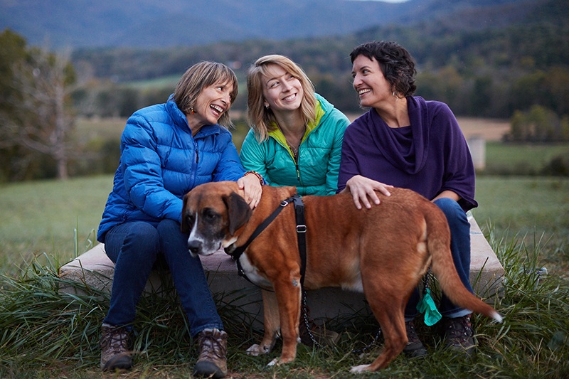 three women laugh with a dog