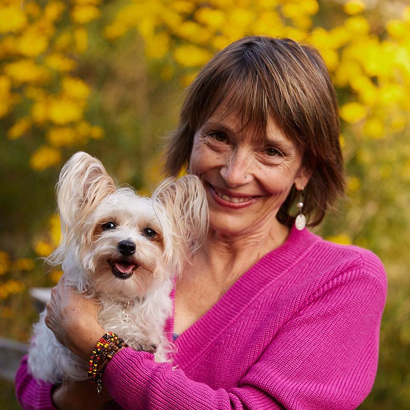 Dr. laurel Davis holds smiling white dog in yellow flowers